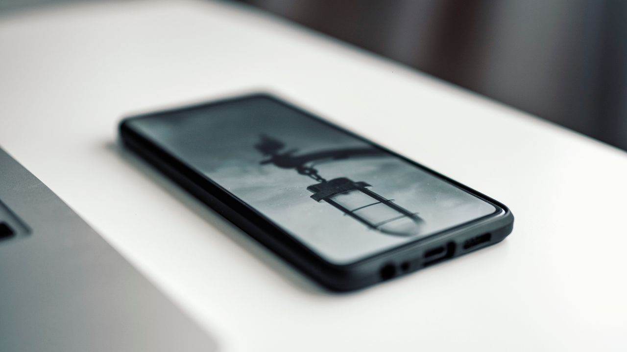 services-01 Close-up of a smartphone showing a blurred image, resting on a desk next to a laptop.